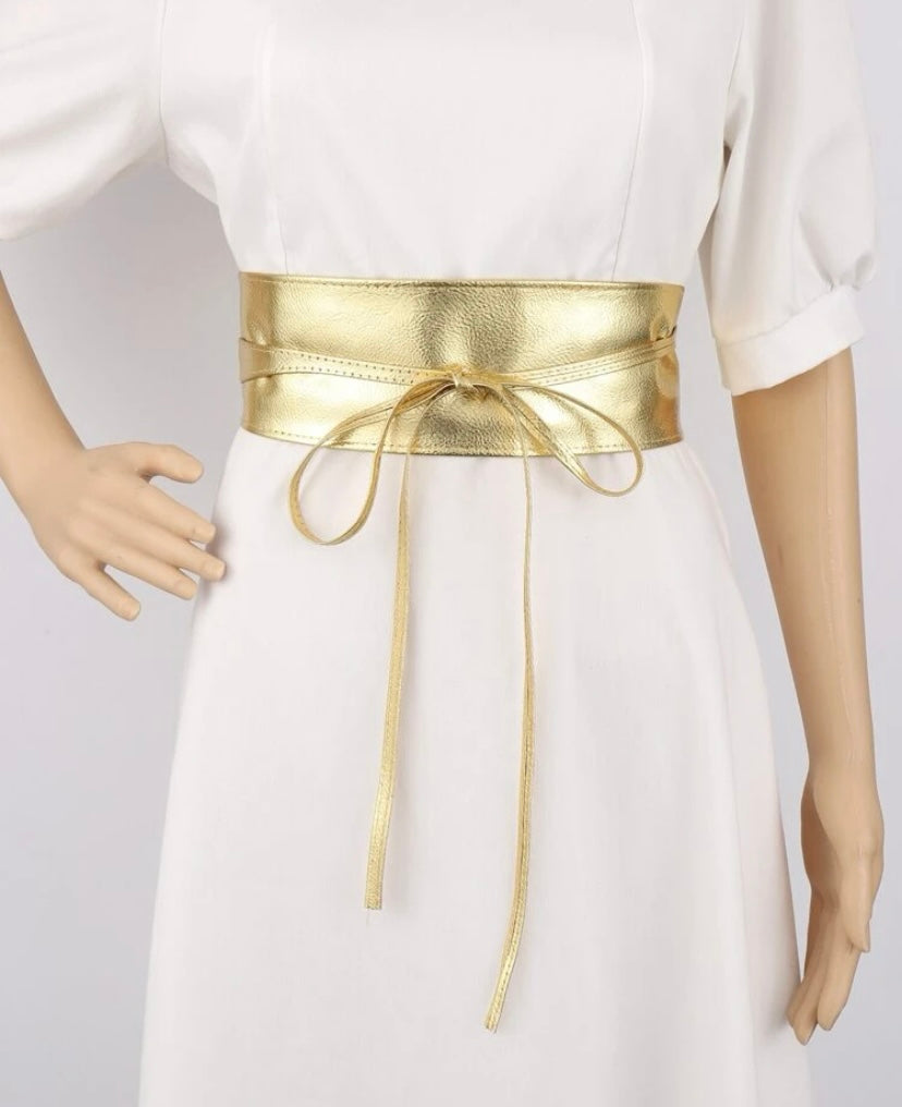 Gold Obi Wrap Belt tied around the waist of a mannequin wearing a white dress, showcasing its shiny metallic finish and elegant design.